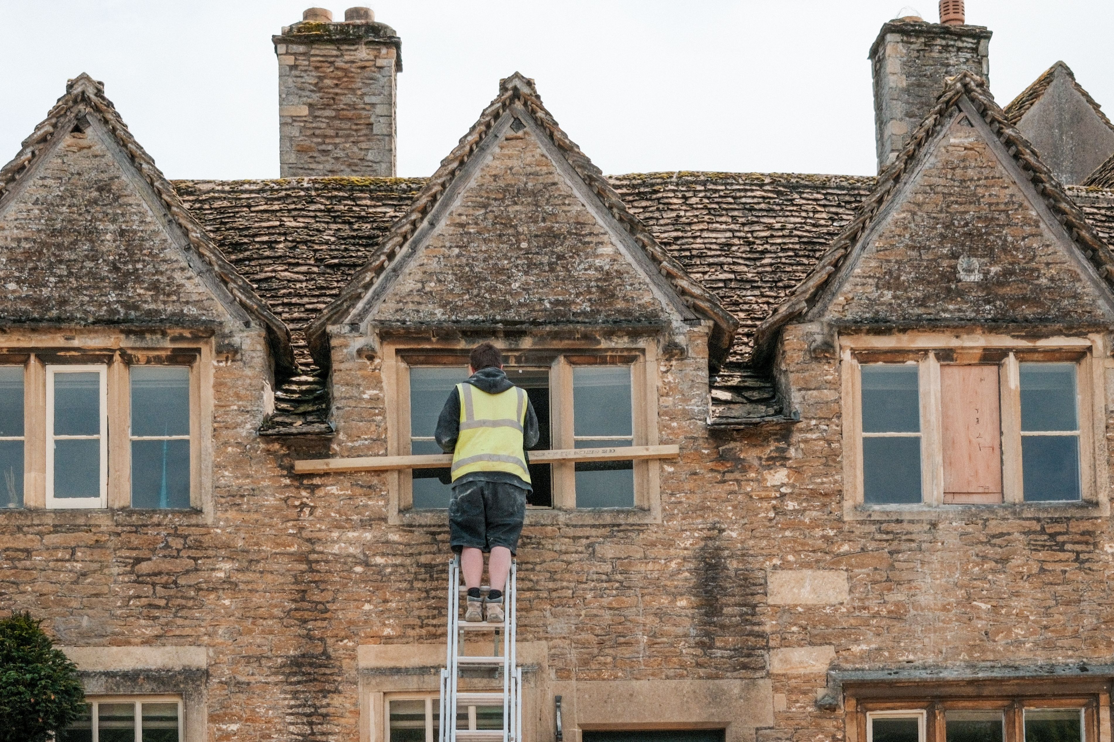 A UK tradesperson on a ladder working on a traditional stone building
